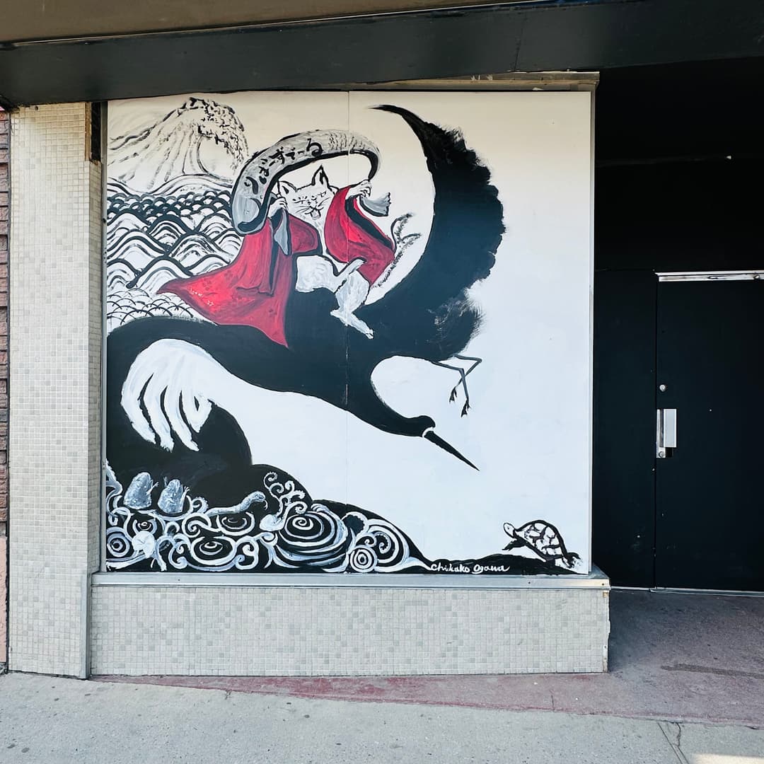 Black and white mural of a cat riding a crane over ocean waves and a turtle
