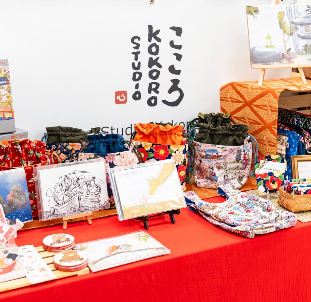 Studio Kokoro branding displayed at a market booth with logo signage, puzzles, and illustrated postcards
