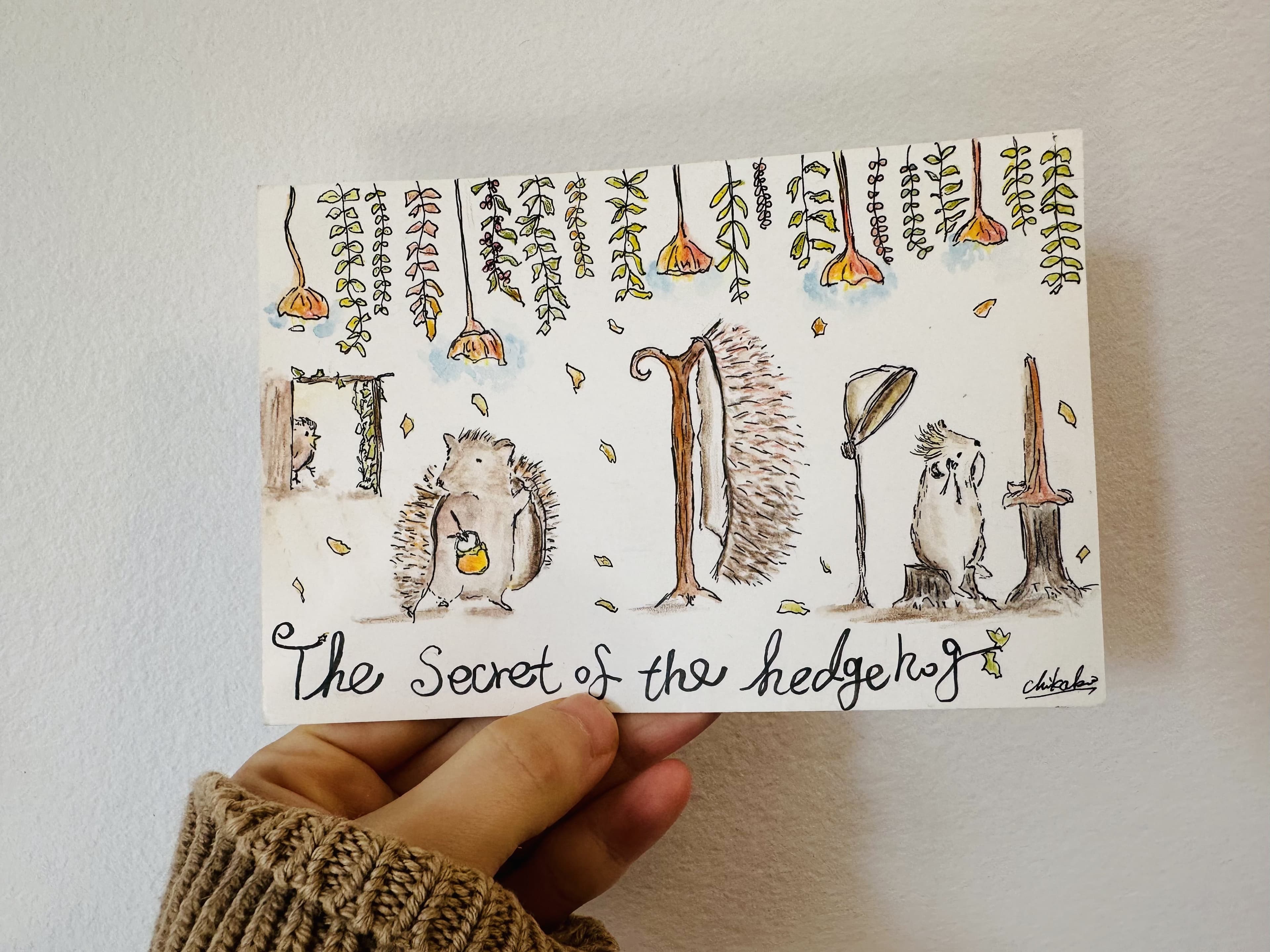 A hand holding a small artwork of a headgehog removing its back needles as a coat