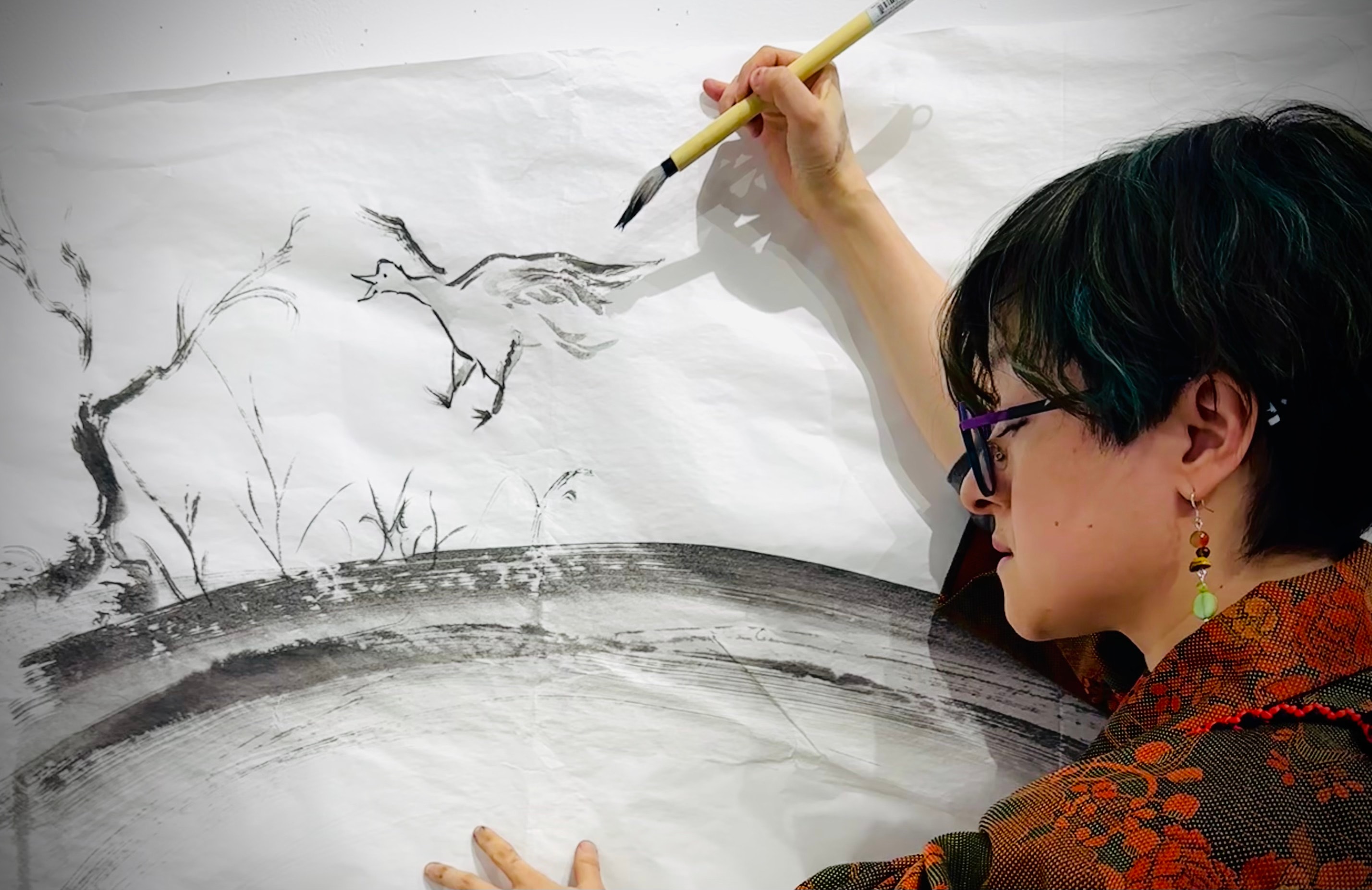 Chikako Ogawa painting a bird and reeds ink illustration on a large paper scroll