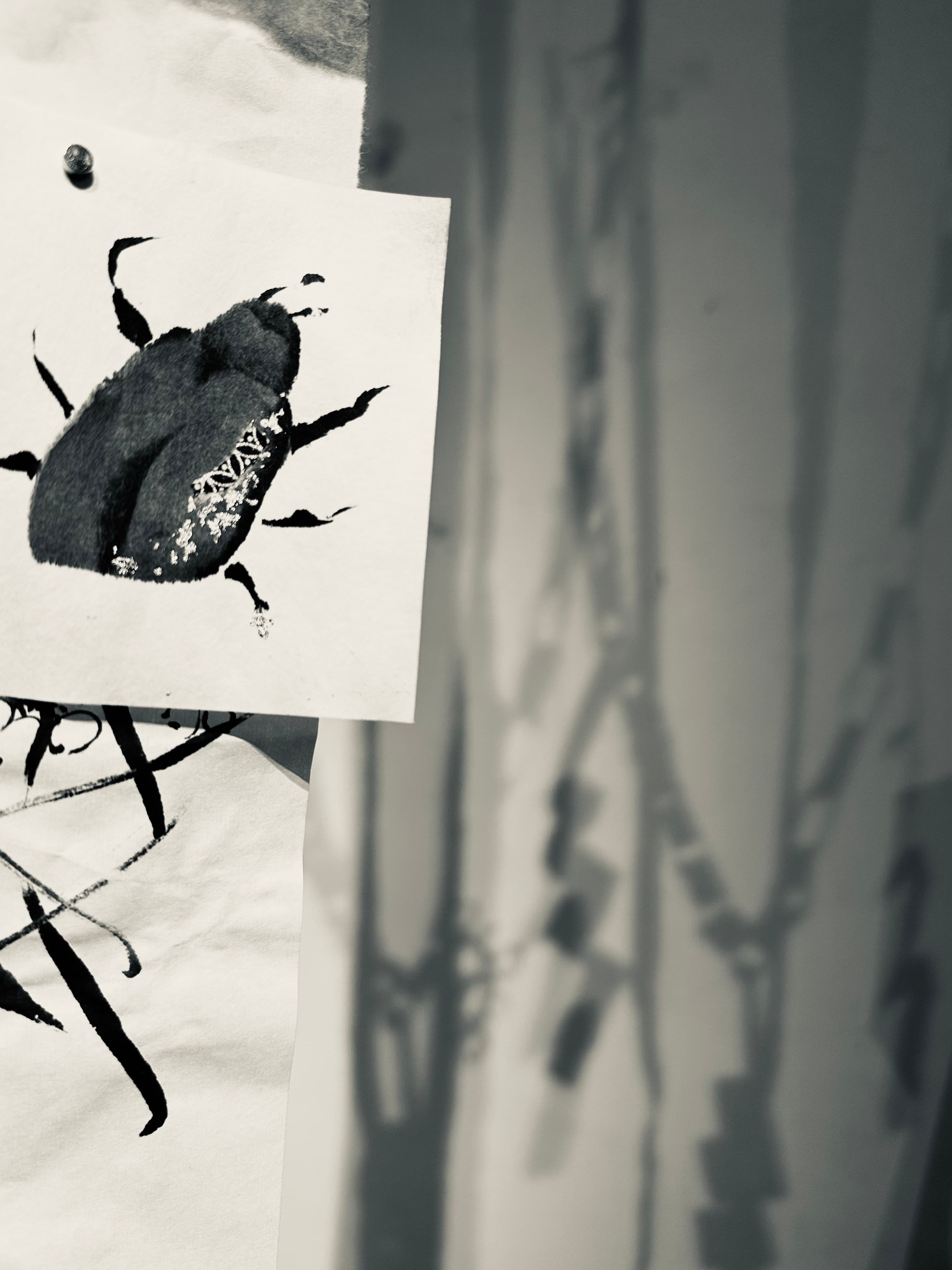 Close-up of a sumi ink painting of a beetle with silver leaf accents, layered over an ink branch sketch